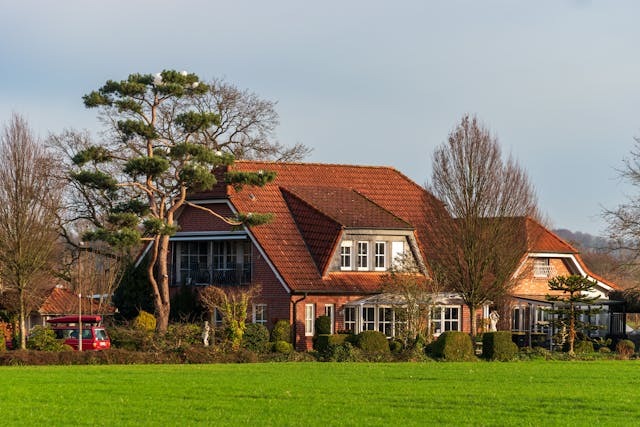 Очарователна червена тухлена къща с балкон, градина и зелена морава.